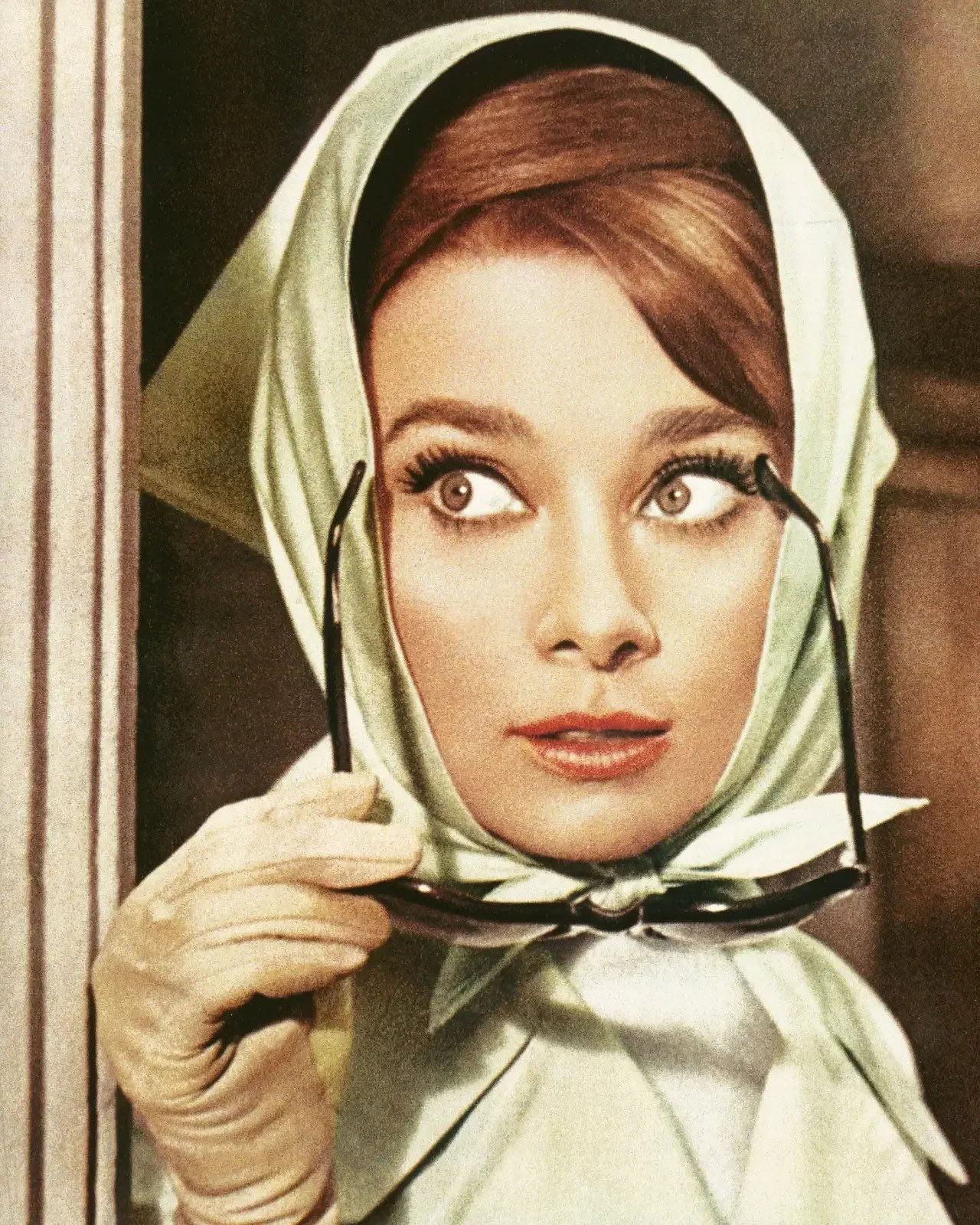 Audrey Hepburn with bug eye glasses in her hand and a bronzed bandana.