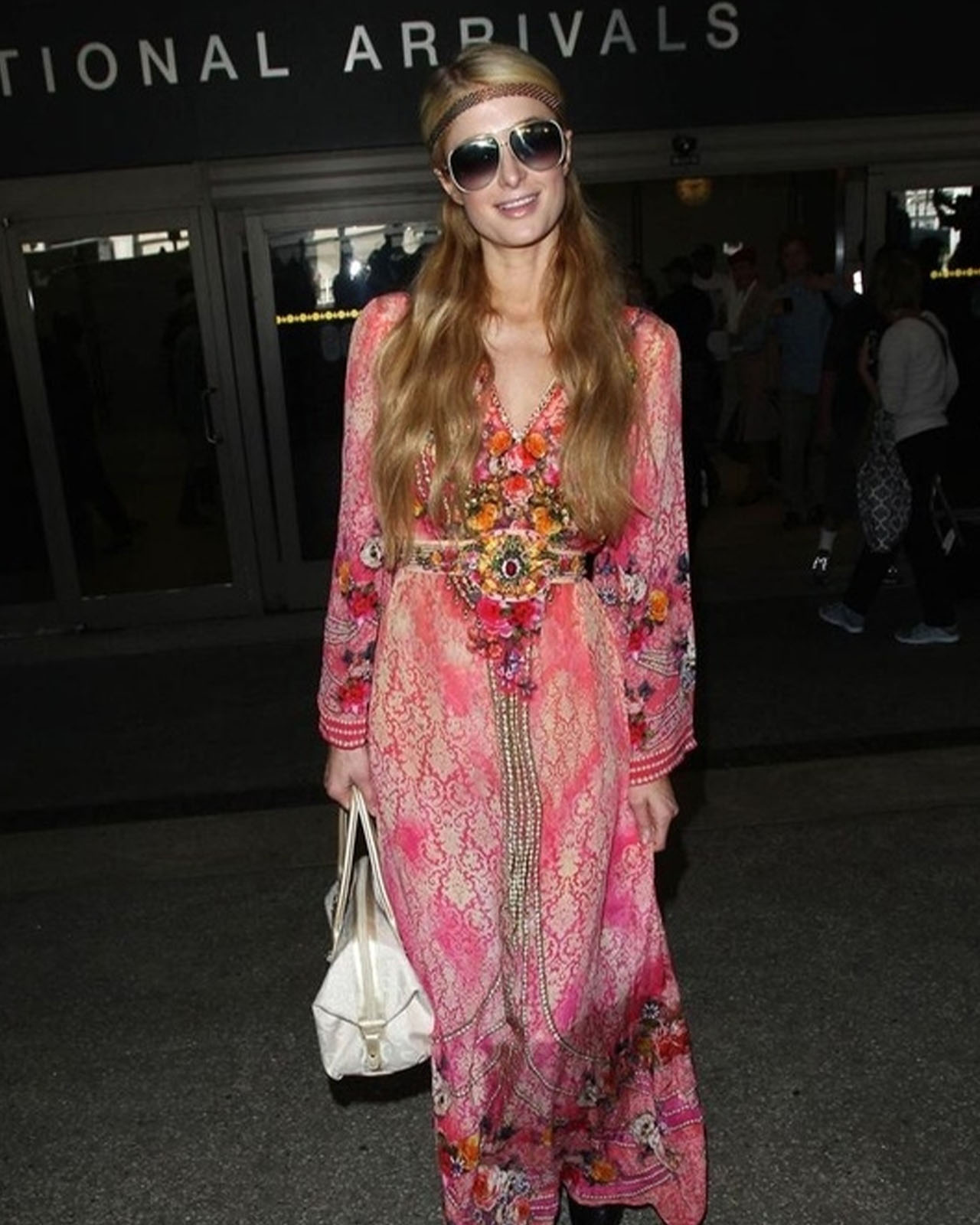Paris Hilton wearing bug eye sunglasses ,wearing a bohemian long dress and carrying a white bag.