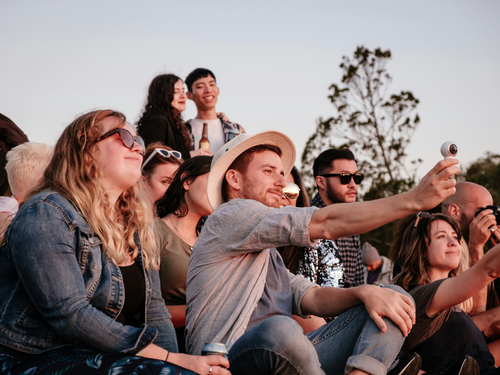 A group of friends sits in a crowd at a music festival, wearing stylish sunglasses for their daytime look.