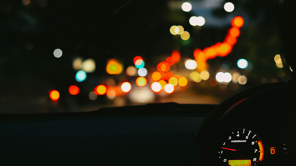 View from inside a car at night showing how traffic lights appear blurry and streaked, demonstrating a common symptom of uncorrected astigmatism.