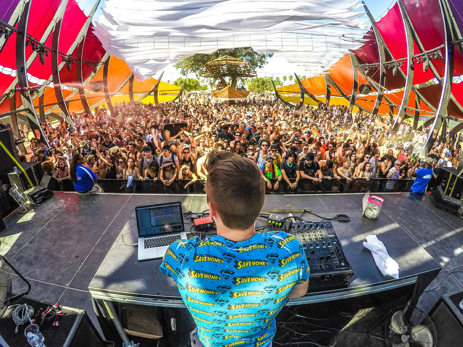 A DJ's view of a large crowd at a sunny outdoor music festival, showing an environment where prescription sunglasses are essential.