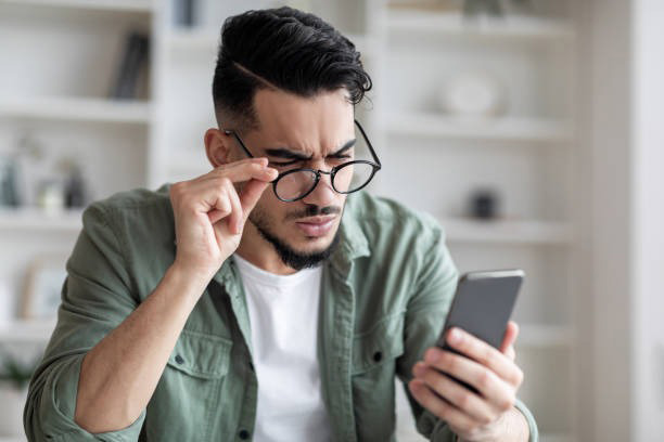 Handsome man wearing farsighted glasses looking at his phone