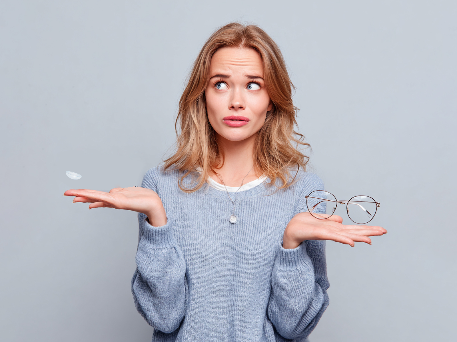 A young woman with a confused expression holds a single contact lens in one hand and a pair of glasses in the other, symbolizing the common question about the differences between eyeglass and contact lens prescriptions.