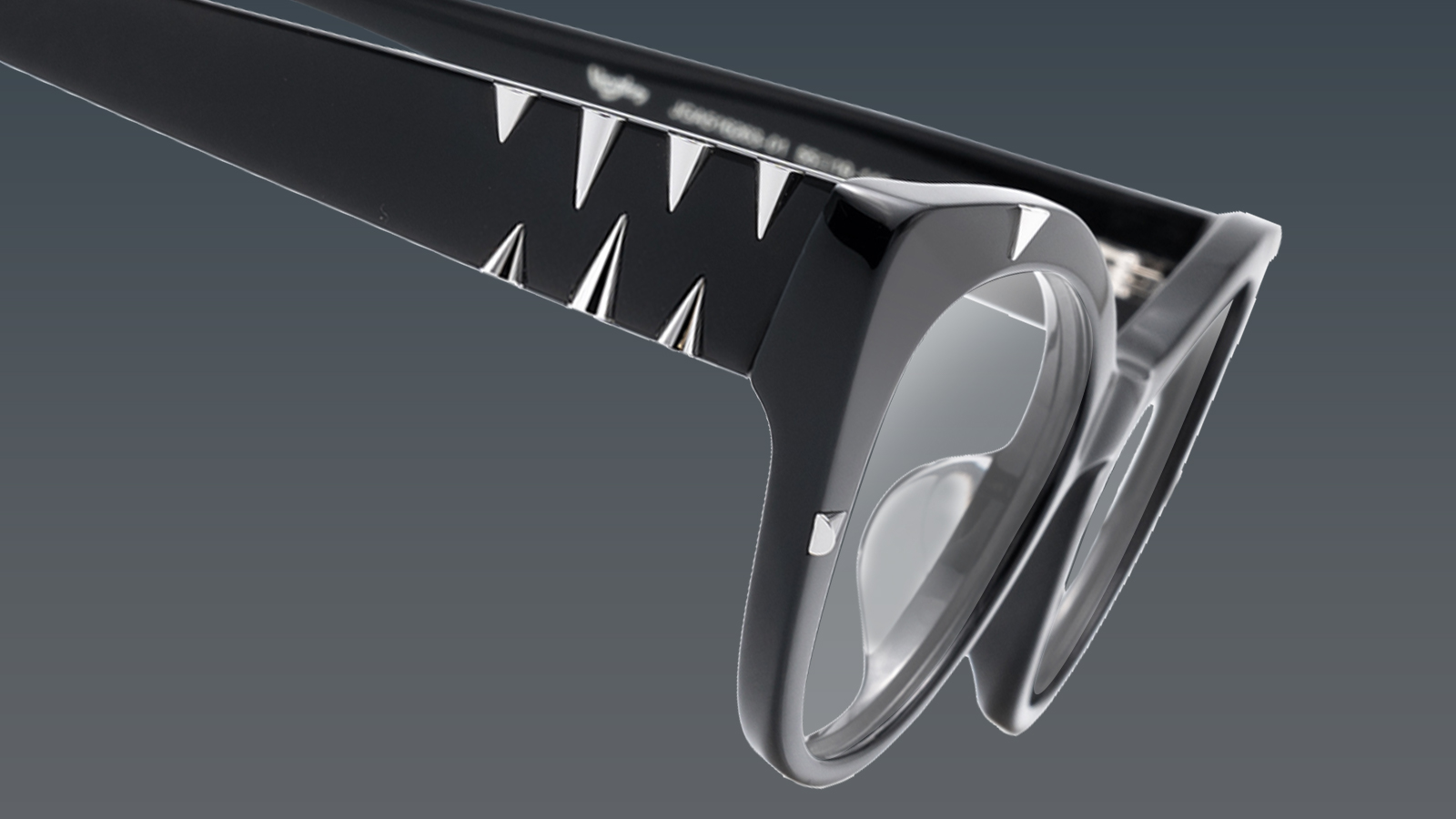 A close-up of bold, black eyeglass frames with sharp silver spikes, representing the avant-garde edge trend for 2026.