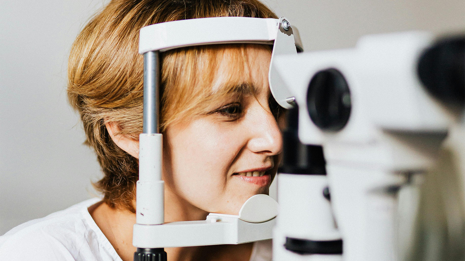 An optometrist conducts a slit lamp eye examination on a young girl, illustrating a key step in the eye exam timeline.
