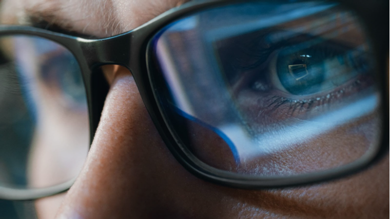 A macro close-up shot of a person's eye looking through a blue light lens, showing a distinct blue reflection on the surface as it filters light.