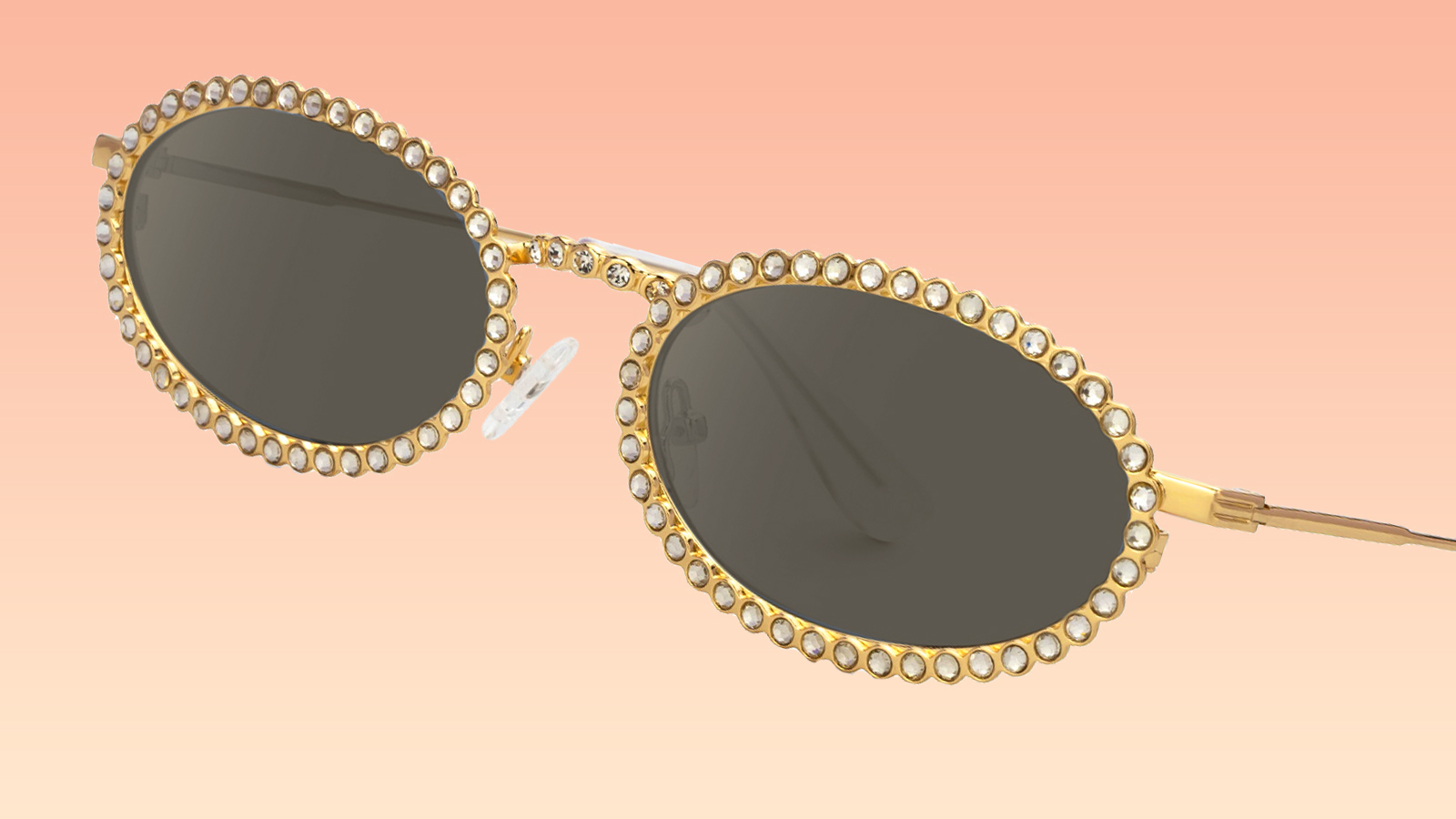 A pair of sleek, 90s-style oval sunglasses with gold frames encrusted in crystals, blending retro and glamour trends for 2026.